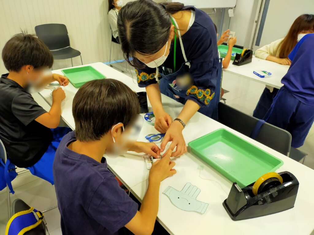 スタッフが子供たちに「ちからクラゲ」の作り方を教えている