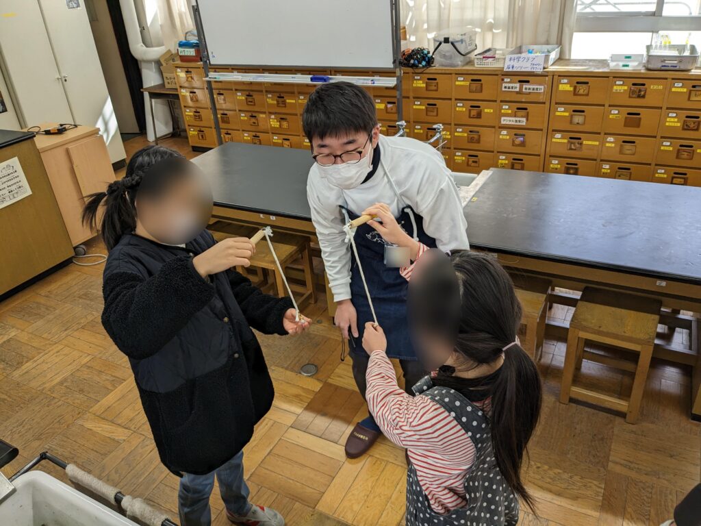 おもりの数を変えてふりこの周期を調べる実験をする子どもと見守るスタッフ